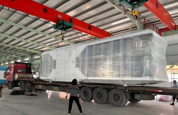 An overhead crane in a factory lifting a wrapped space capsule cabin onto a flatbed trailer, illustrating the initial stage of OOG logistics