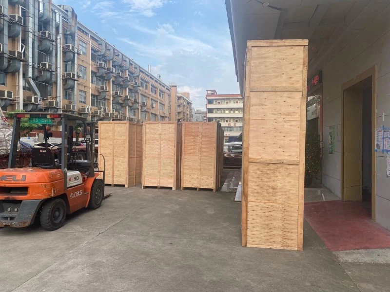 Orange forklift maneuvering tall plywood export crates outside factory building, demonstrating logistics readiness and material handling safety