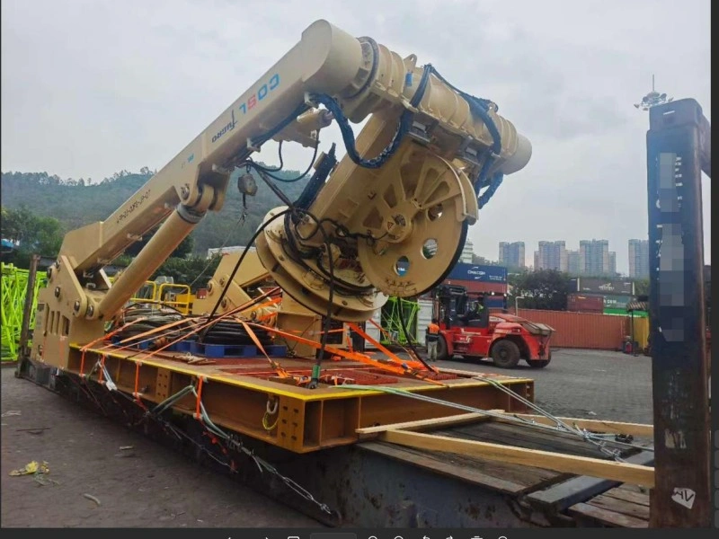 A large yellow drilling rig component, labeled “T500”, is securely strapped with orange lashing belts onto a flat rack container at a logistics yard, with a red forklift and shipping containers visible in the background.