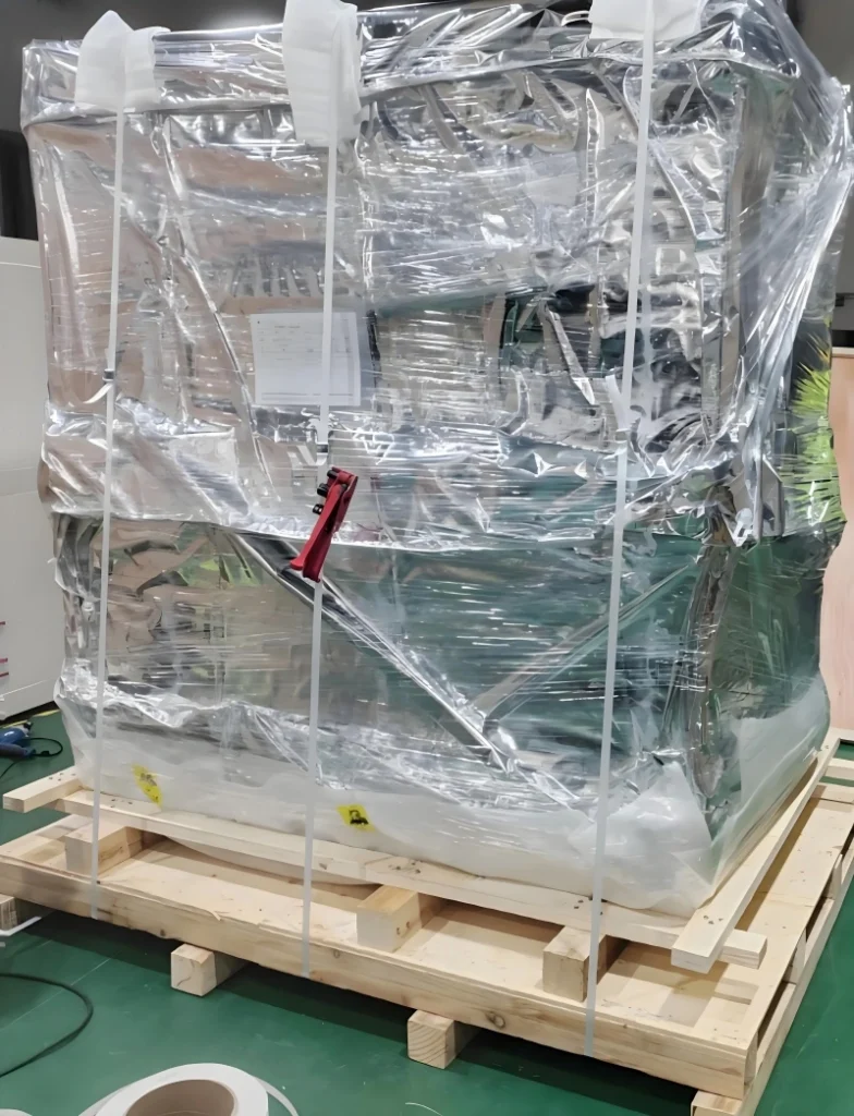 Blue machinery unit tightly wrapped in transparent protective film with white lashing straps and red tensioner, showing correct strapping technique to avoid seam compression during container loading.