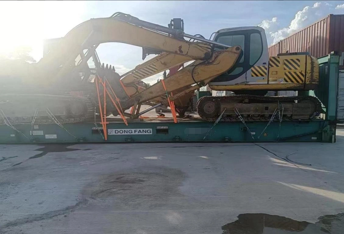 A large yellow tracked excavator secured on a green flat rack container at a logistics yard, with Maersk containers in the background, demonstrating heavy machinery transport solutions.
