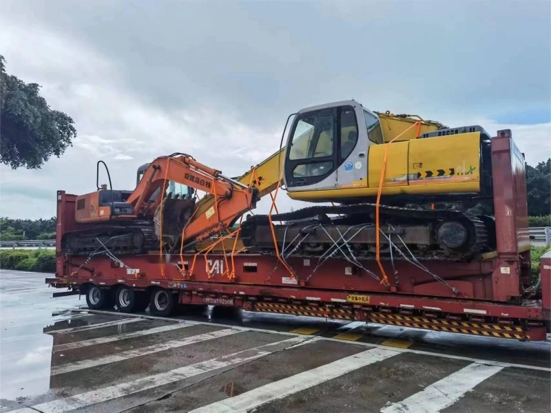 Two heavy excavators, one yellow and one orange, securely strapped onto a red lowbed flatbed trailer for long-distance transport.