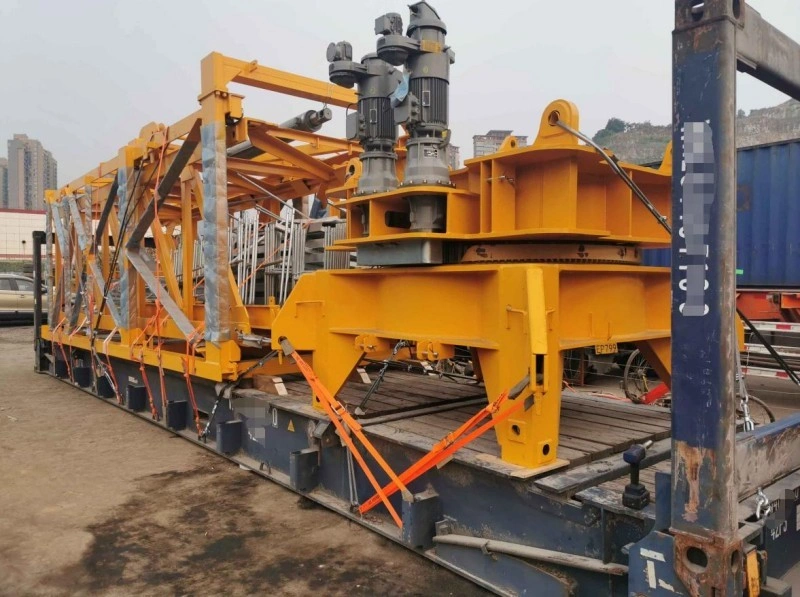 A large yellow industrial machine with motors and steel framework is tightly secured to a blue flat rack container using orange lashing straps and wooden dunnage for stability.