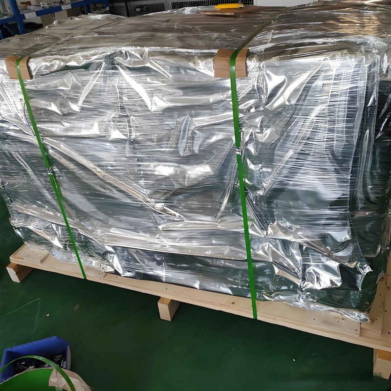 Large industrial equipment wrapped in reflective aluminum foil vacuum bag on wooden pallet, secured with green strapping bands for moisture and corrosion resistance during sea transport.