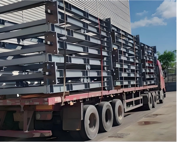 Flatbed truck loaded with stacked black steel beams and columns, demonstrating optimized space utilization and secure stacking for structural steel delivery.