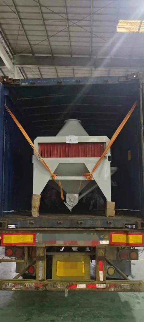 Rear view of a large industrial dust collector with red filter bags secured inside a blue open top shipping container using orange heavy-duty lashing straps, ready for road transport.
