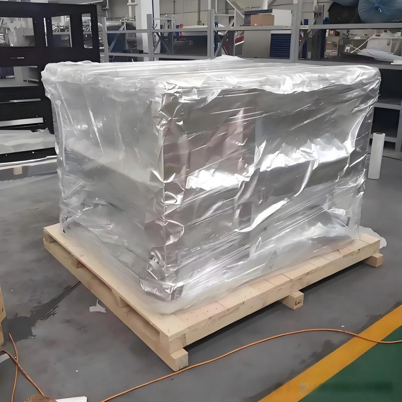 A large industrial machine wrapped in reflective aluminum foil barrier film and secured with orange straps on a wooden pallet, demonstrating vacuum packaging for moisture and corrosion prevention during sea freight.
