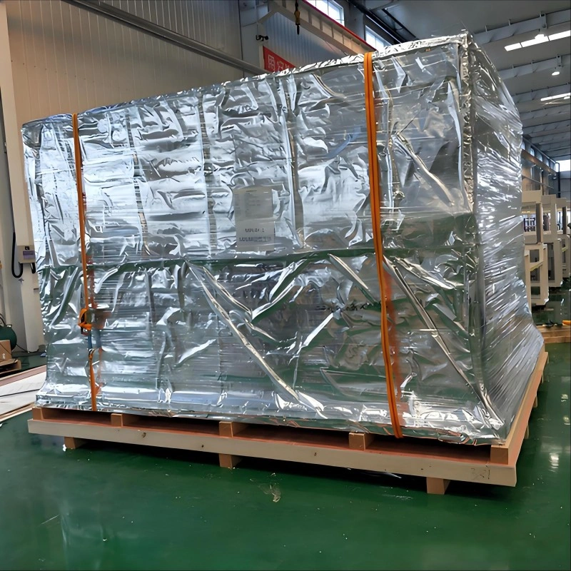 A large industrial machine wrapped in reflective aluminum foil barrier film and secured with orange straps on a wooden pallet, demonstrating vacuum packaging for moisture and corrosion prevention during sea freight.
