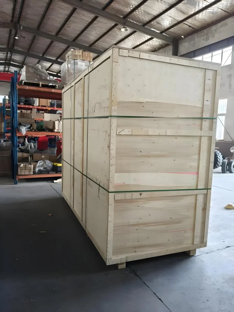 A tall, fully assembled plywood export crate secured with green strapping bands inside a factory warehouse, ready for shipment of oversized industrial goods.