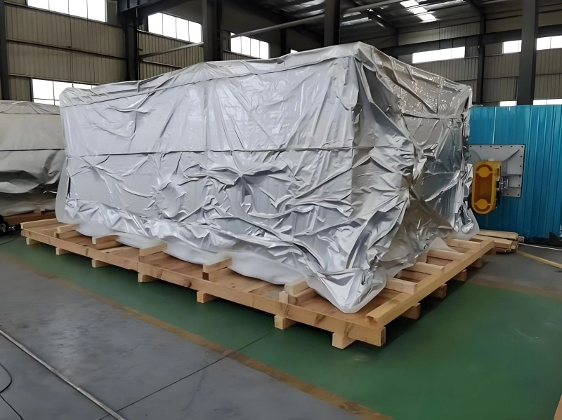 A bulky piece of industrial equipment fully encased in reflective aluminum foil vacuum packaging, resting on a wooden pallet inside a warehouse, showcasing advanced moisture and corrosion protection for high-value machinery.