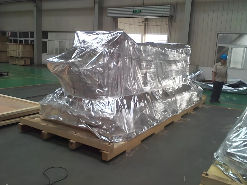 A bulky piece of industrial equipment fully encased in reflective aluminum foil vacuum packaging, resting on a wooden pallet inside a warehouse, showcasing advanced moisture and corrosion protection for export.