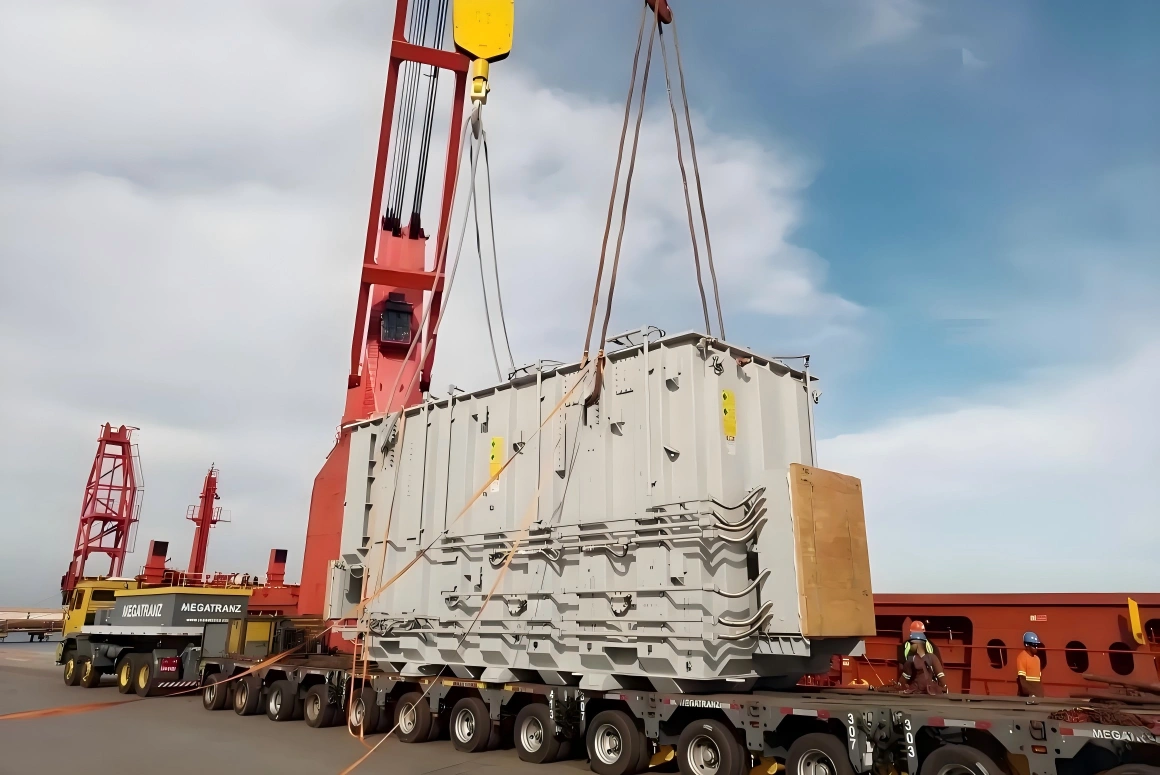 Large red harbor crane lifting a massive power transformer onto a ship deck, illustrating the final stage of multimodal OOG logistics