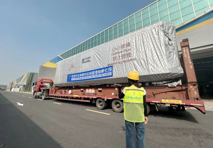 A logistics worker in a yellow safety vest supervising the loading of a fully furnished space capsule cabin onto a flatbed trailer for OOG transport