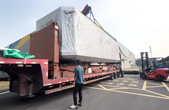 A worker observing a wrapped space capsule cabin on a flatbed trailer, with a forklift nearby, highlighting the coordination involved in OOG logistics