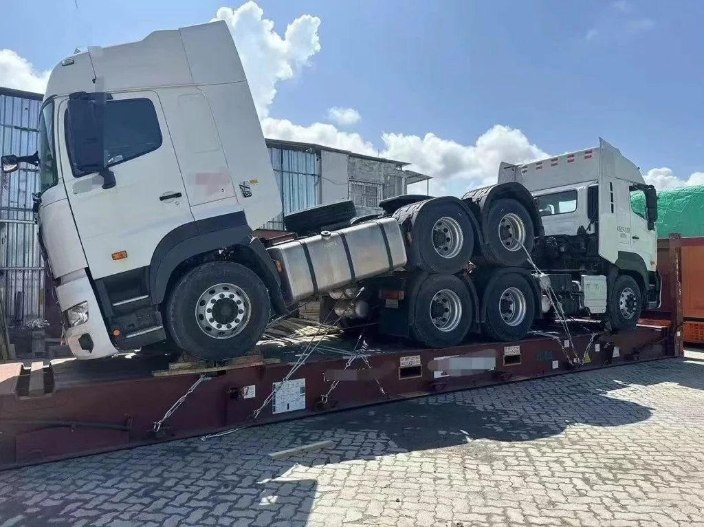 Two white heavy-duty tractor heads loaded on a flat rack container, illustrating the complexity of oversized cargo logistics and the need for early planning to avoid rush fees.