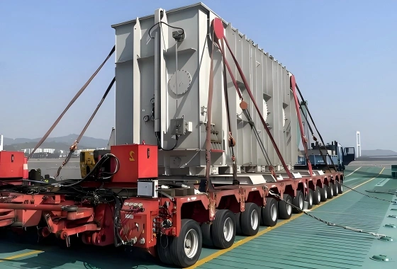 Red self-propelled modular transporter (SPMT) moving a heavy power transformer at a port facility, showcasing stability and control for OOG cargo