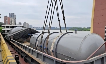 Crane lifting a large pressure vessel onto a transport barge or ship, illustrating the coordinated port handling required for OOG cargo export.