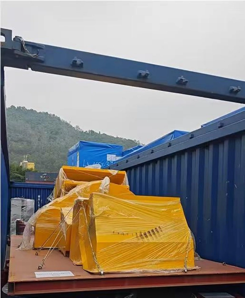 Yellow industrial parts wrapped in clear stretch film being loaded onto a blue flat rack container using overhead lifting gear, highlighting careful handling procedures for fragile manufacturing assets.