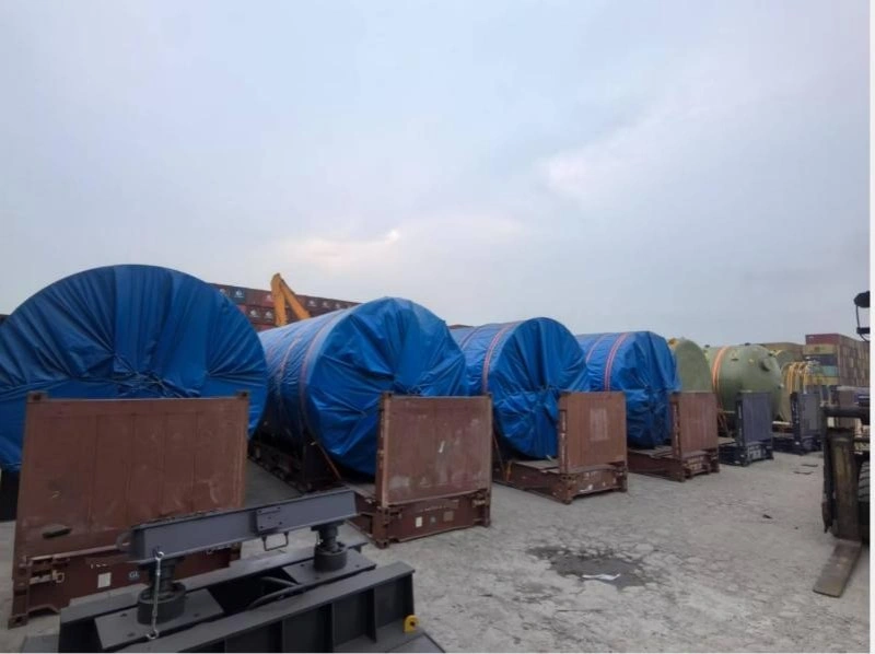 Multiple large cylindrical tanks wrapped in blue protective covers, staged on flatbed trailers at a logistics yard, illustrating pre-move preparation for high-value production line equipment.