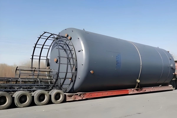Grey pressure vessel loaded on a flatbed trailer with protective framing, ready for inland transportation and export logistics.