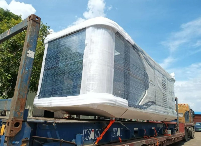 A prefabricated space cabin module wrapped in clear plastic film and secured with orange straps on a flatbed trailer, prepared for safe relocation.