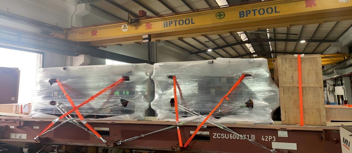 Two large molds wrapped in protective plastic and secured with reinforced orange lashing straps for stability during OOG transport.
