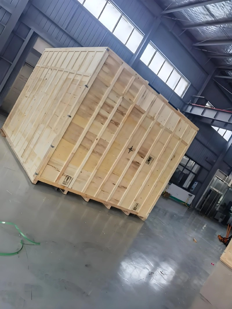A large, custom-built plywood export crate featuring external wooden framing and corner reinforcements, positioned inside a warehouse to showcase heavy-duty packaging for industrial equipment.