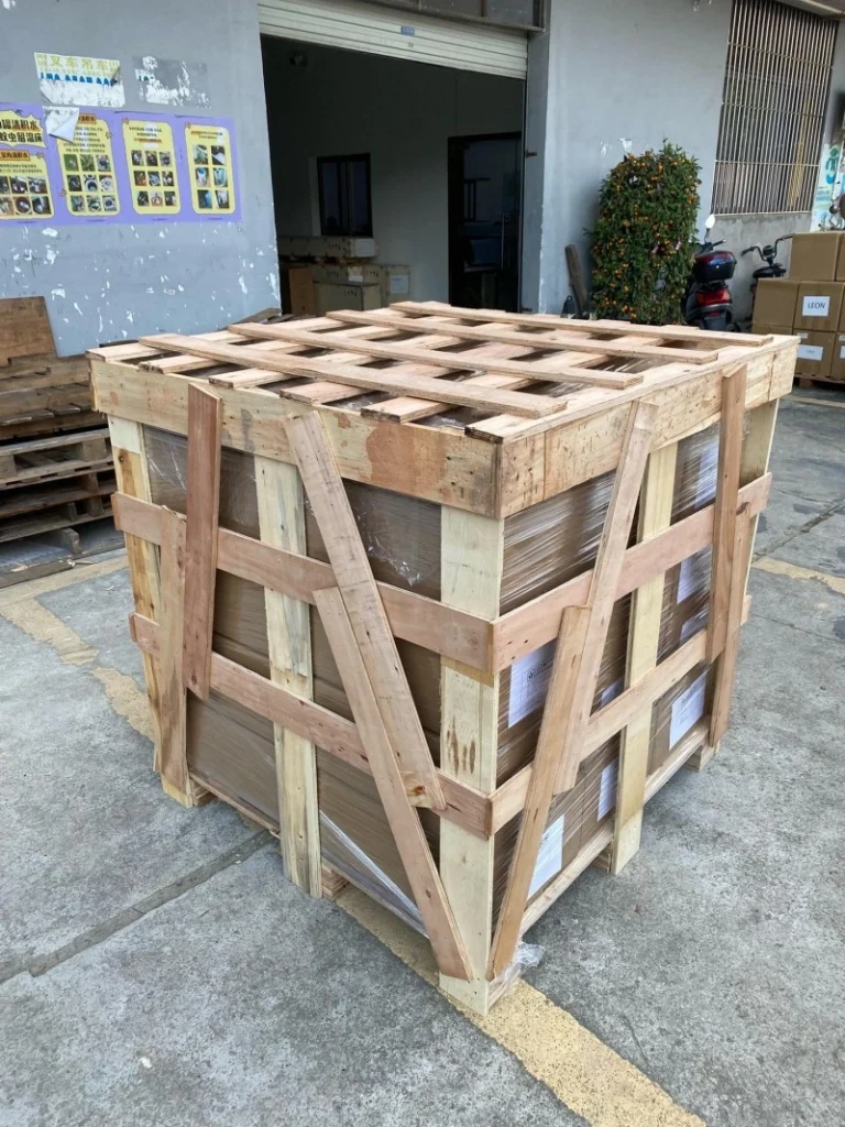 Tall wooden export crate with diagonal cross-bracing and plastic-wrapped contents, demonstrating vibration isolation and ESD-safe handling for control panels