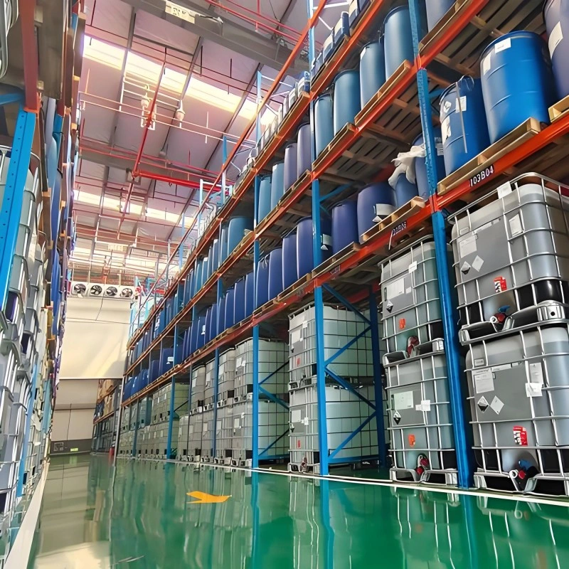 Blue industrial racking system storing compressed gas cylinders. The lower shelves hold cylinders in grey metal safety cages with red tops and hazard warning labels, while the upper shelves have cylinders secured in wooden crates. The location is marked with aisle identifiers like "101B04".