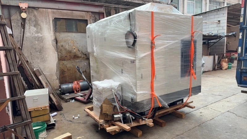 An industrial machine wrapped in clear plastic film and secured with orange straps on a wooden pallet, prepared for safe relocation.