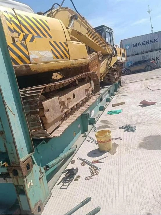 Side view of a yellow excavator firmly strapped with orange lashing belts on a Dong Fang branded flat rack container, ready for multimodal logistics shipment under bright sunlight.