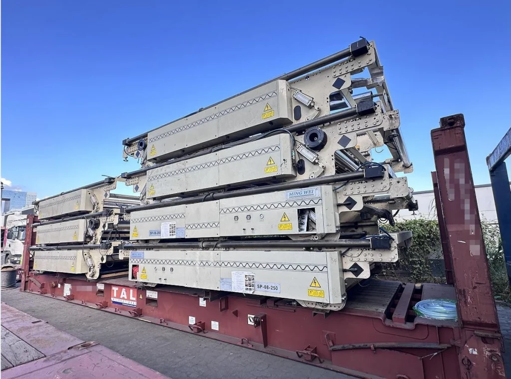 Multiple beige industrial press units labeled “MING WEI” and “SP-08-250”, stacked vertically and secured with straps on a red flat rack container, under clear blue sky at a port yard.