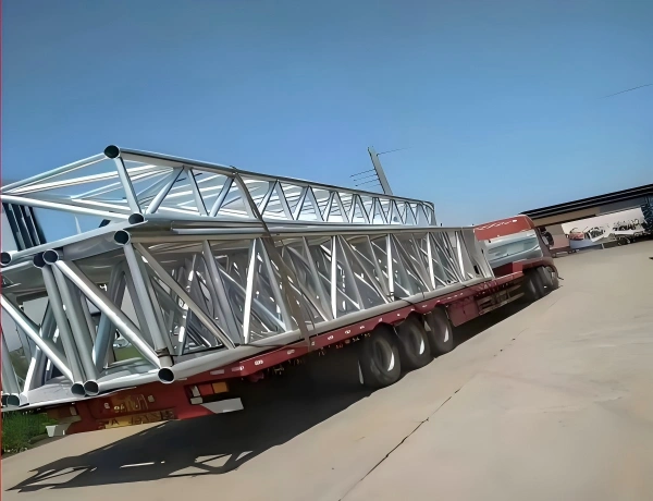 Flatbed trailer transporting large, fabricated silver steel truss structures, demonstrating specialized handling for long and oversized OOG cargo.