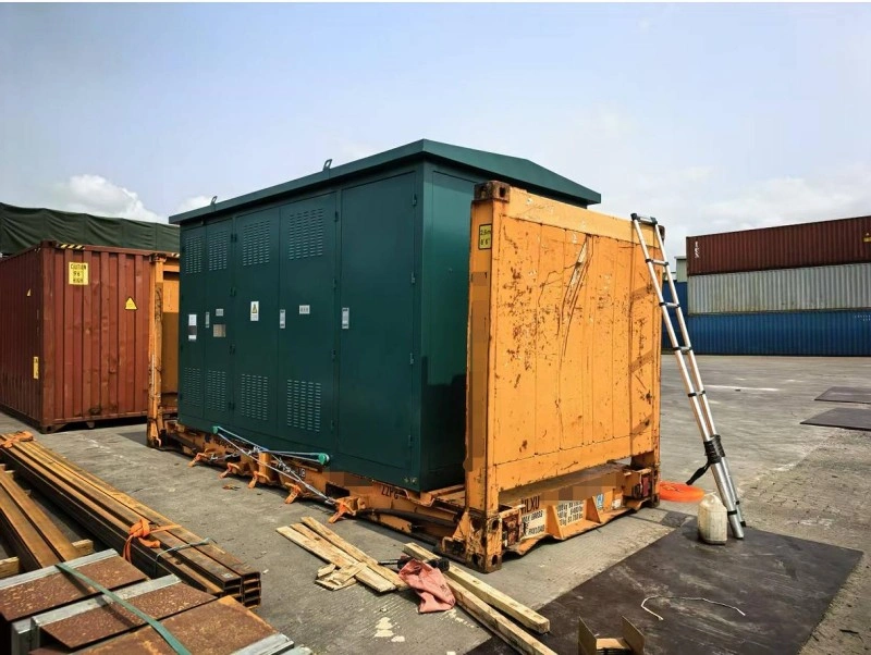 A dark green metal enclosure, likely housing electrical or control systems, is positioned on a weathered yellow flat rack container; a telescoping ladder leans against its side, suggesting ongoing inspection or preparation for loading/unloading at a port facility.