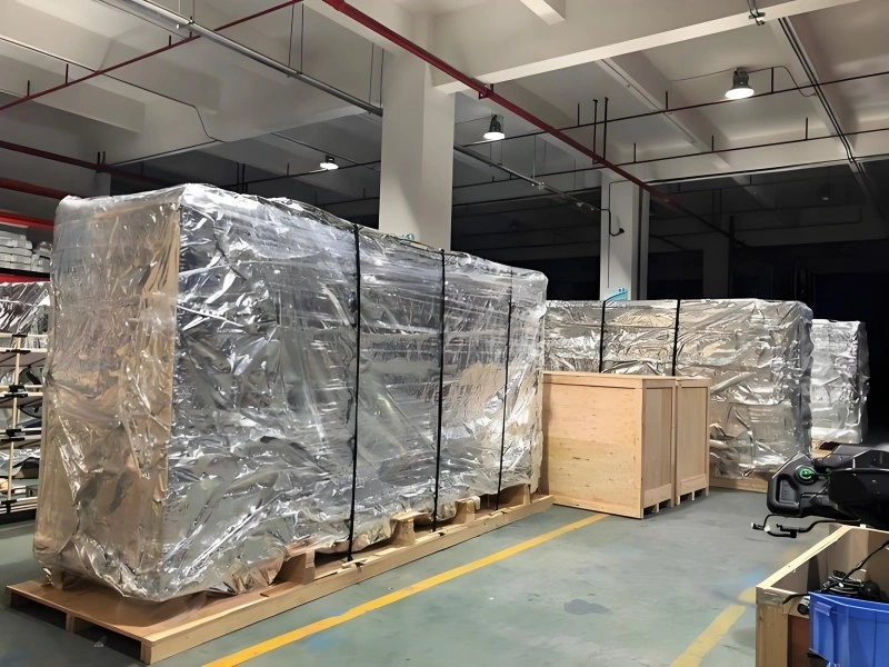 Multiple units of industrial equipment sealed in reflective aluminum foil vacuum bags are stored on pallets inside a modern warehouse, demonstrating layered packaging for corrosion and moisture prevention.