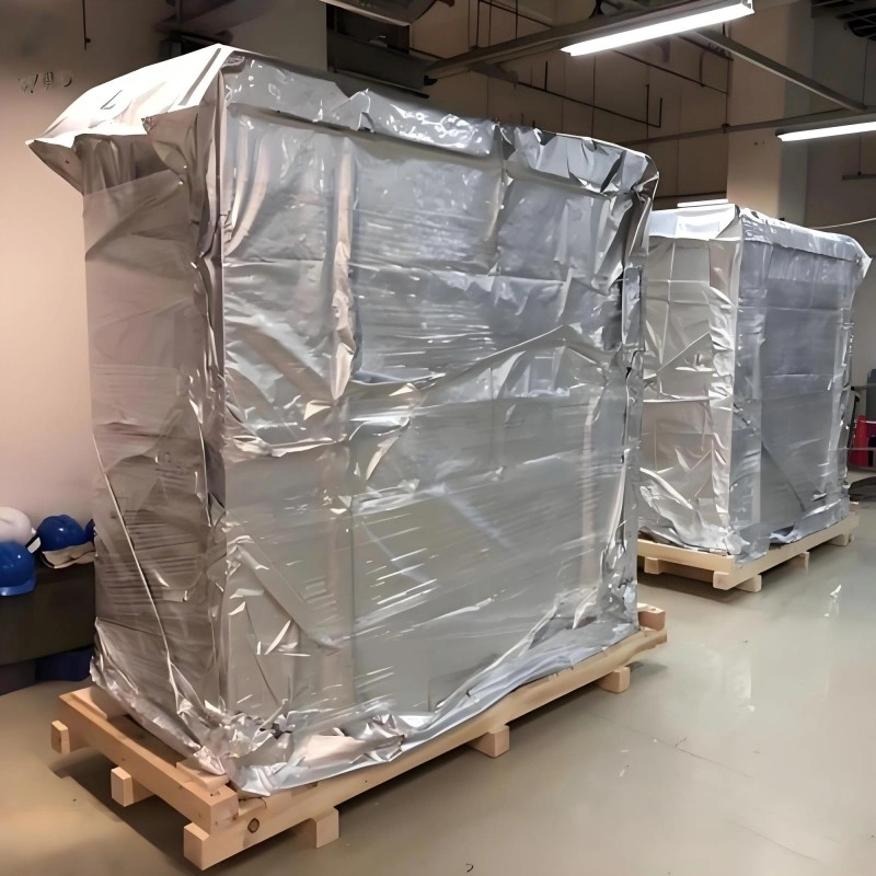 Large industrial machine wrapped in reflective aluminum foil vacuum bag on wooden skid, demonstrating proper packaging design to prevent seal damage during warehouse handling and ocean freight.