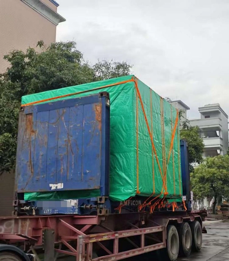 A large cargo container covered with a green waterproof tarp and secured with orange straps on a flatbed trailer, prepared for outdoor transport.