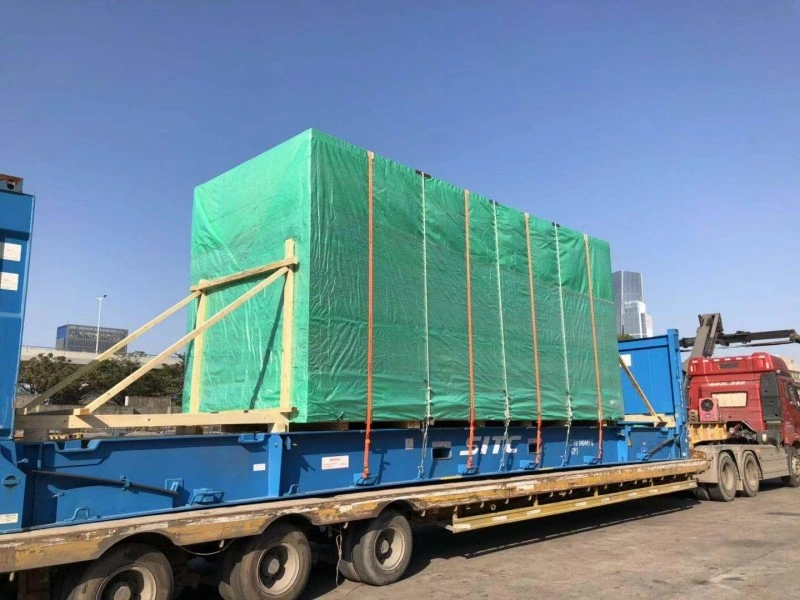 Two logistics workers wearing yellow hard hats and high-visibility vests with the "Bentlee" logo are tightening steel wire ropes to secure a long, silver-wrapped cargo item onto a large red trailer or container base. The cargo is covered in protective plastic wrap.