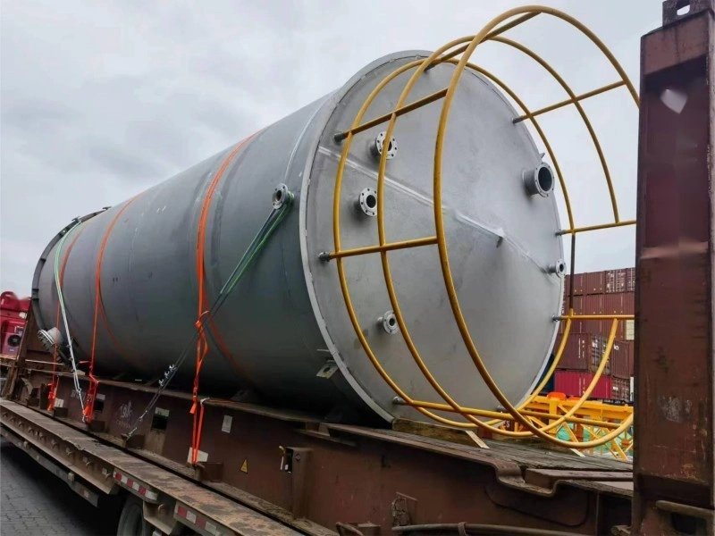 Close-up of yellow safety cage and orange lashing straps securing the end of a large industrial tank on a flat rack trailer