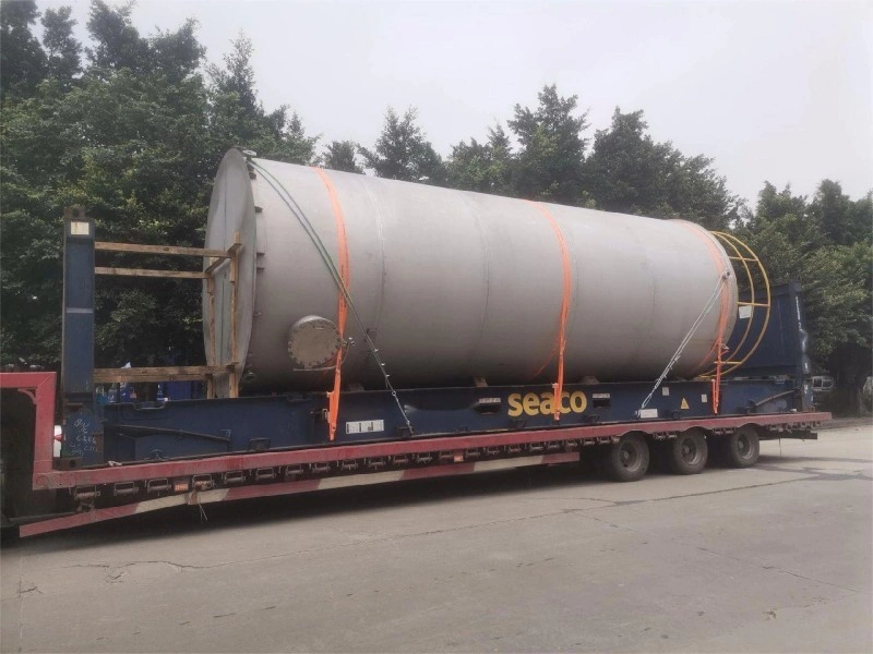 Large cylindrical stainless steel tank secured with orange straps on a blue Seaco flat rack container for multimodal transport