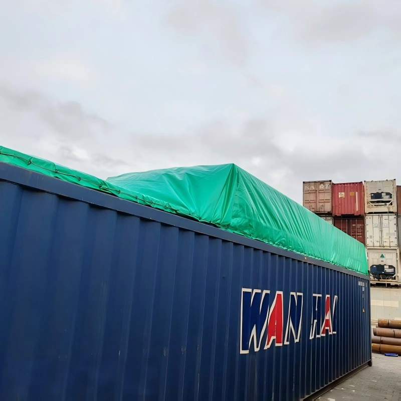 Blue Wan Hai open top container with green tarp cover, viewed from the side, with stacked shipping containers in the background